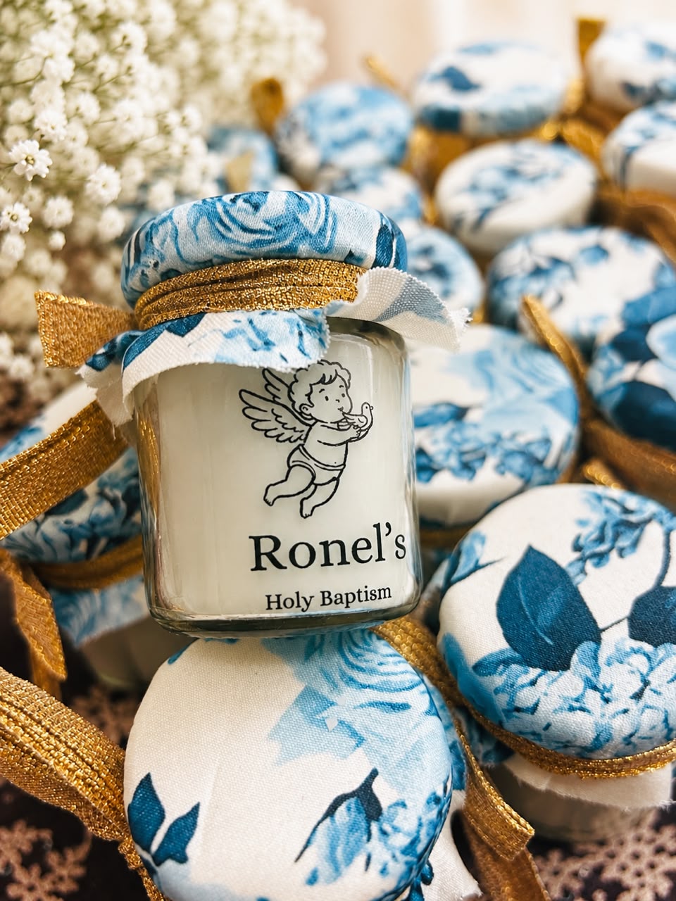 Mini jar candle return favours for a baptism, capped in blue floral fabric with gold ribbon